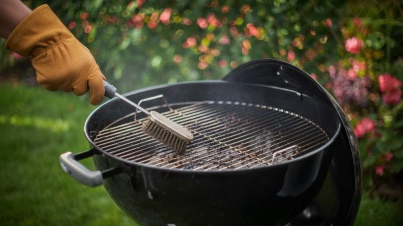 Weber Original Kettle 22-Inch charcoal grill with cooking grate being brushed clean after use