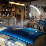 Beginner using an HVLP spray gun to paint a car panel in a home garage