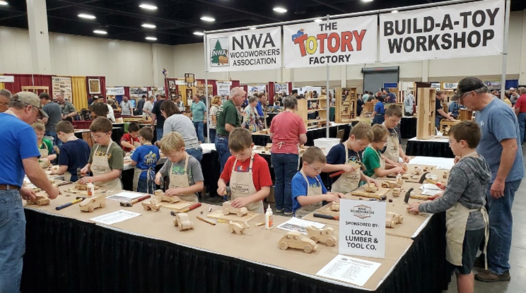 Children building wooden toys at the Toy Factory booth during the NWA Woodworking Show April 2027